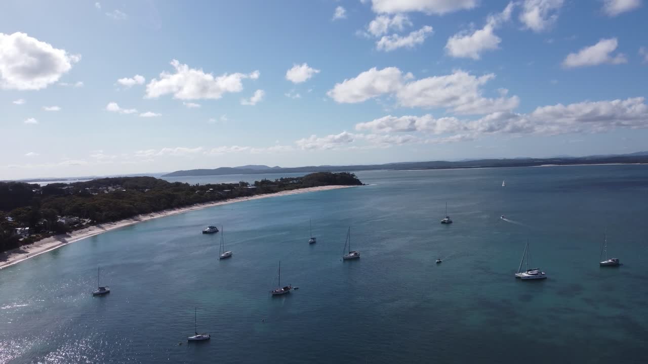 Drone flyver over sejlbåde mod en hvid sandstrand