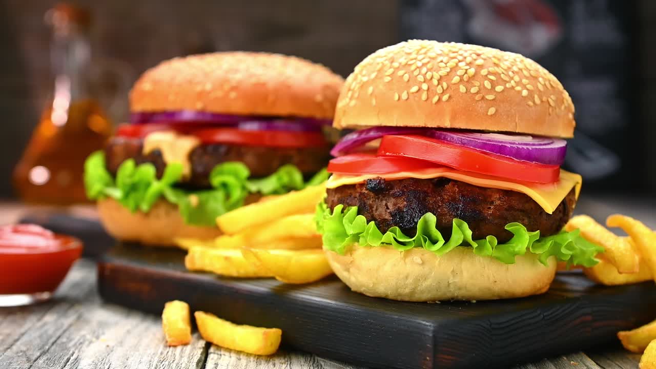 Deliziosi hamburger con patatine fritte serviti su un tagliere di legno in un ristorante informale. Due hamburger con formaggio, lattuga, pomodori e cipolle sono disposti su un tagliere di legno accanto a una porzione di patatine fritte.