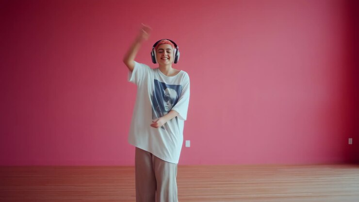 A happy person with pink hair and headphones dancing in a pink room