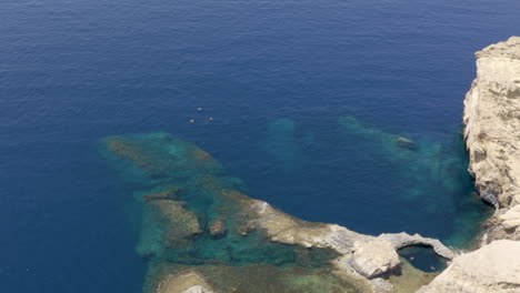 Group-of-scuba-divers-diving-under-a-rocky-cliff-next-to-a-rock,aerial