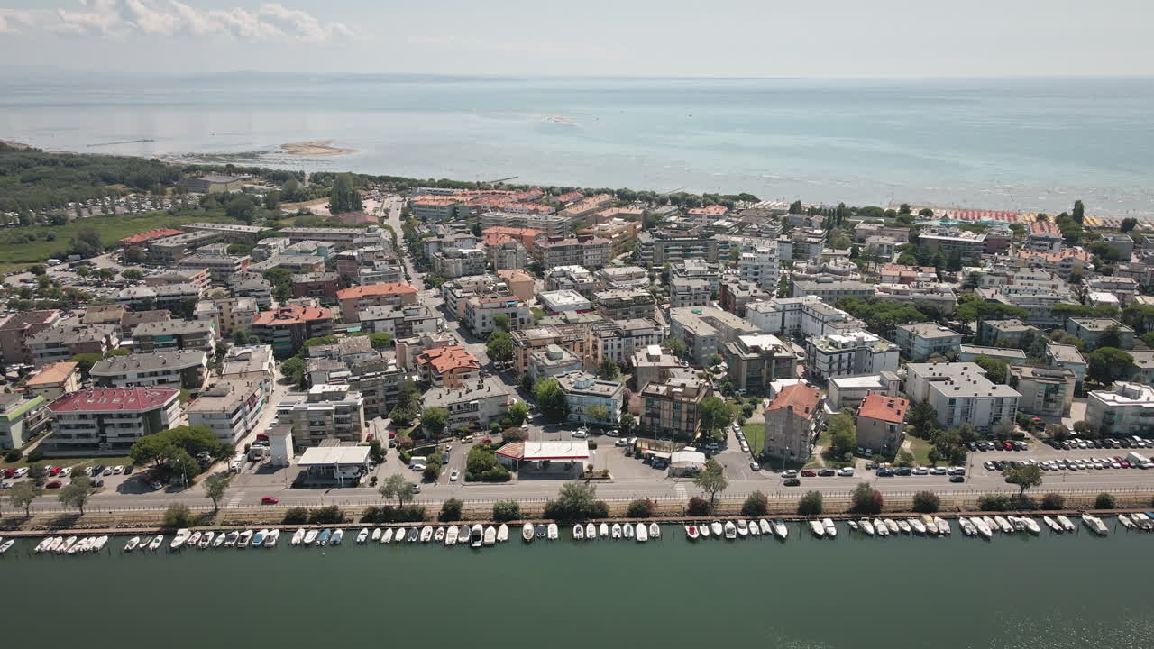 Smooth 4K UHD drone pulls back from a dense Grado residential area, revealing the town's grid and the vast surrounding lagoon—ideal for travel films and establishing sequences