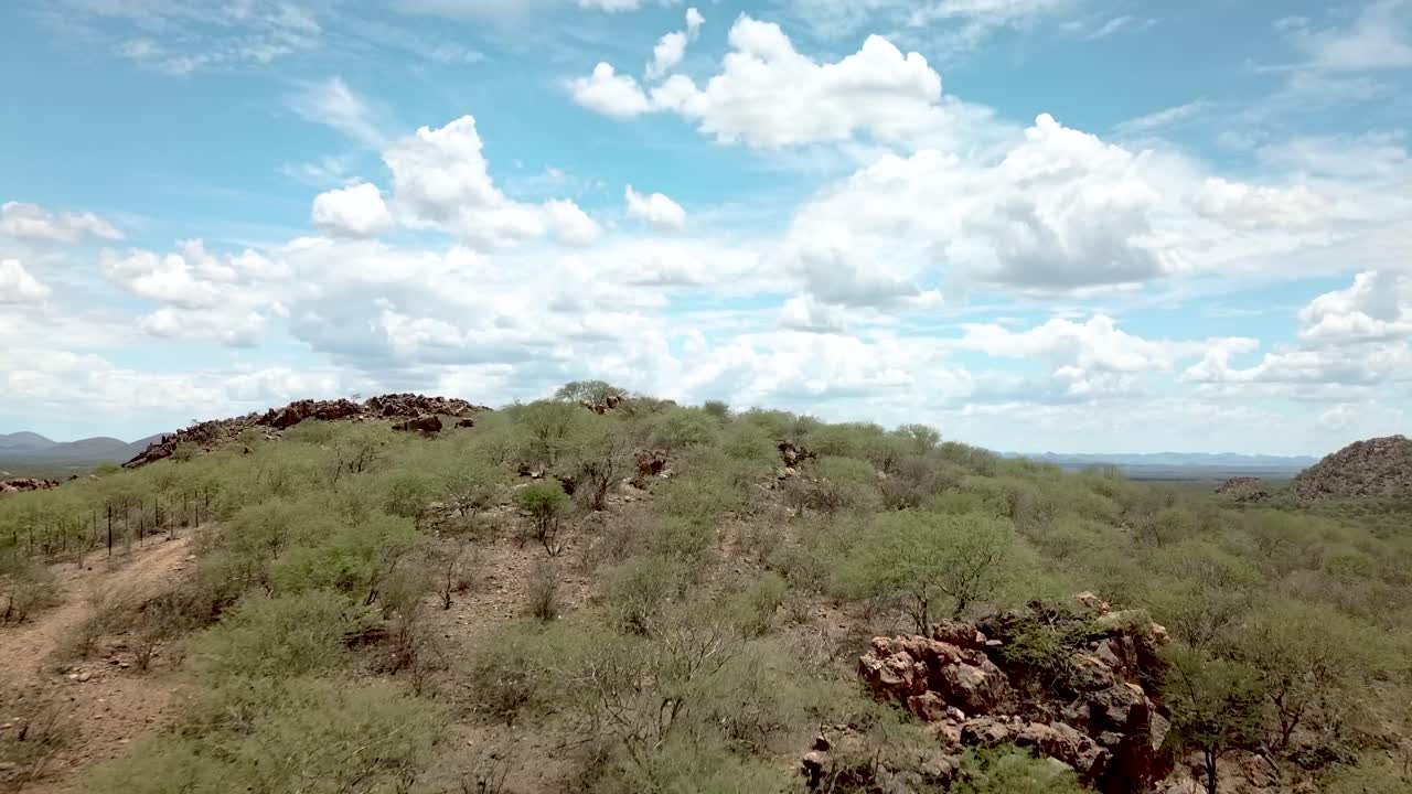 나미비아의 오카한자 근처의 건조한 야생 동물 농장에서 산 위에서 촬영된 전진하는 드론, 광활한 풍경을 보여줍니다.