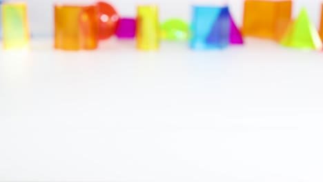 a hand interacts with colorful 3d geometric shapes on a white surface, highlighting educational and playful elements