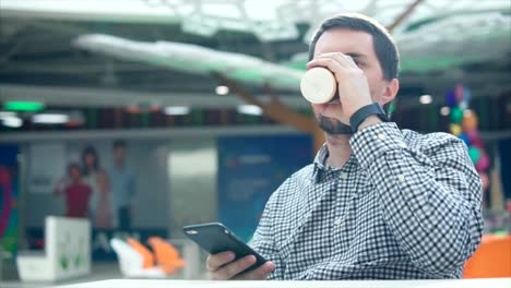man drinking coffee and using a smartphone in a shopping mall