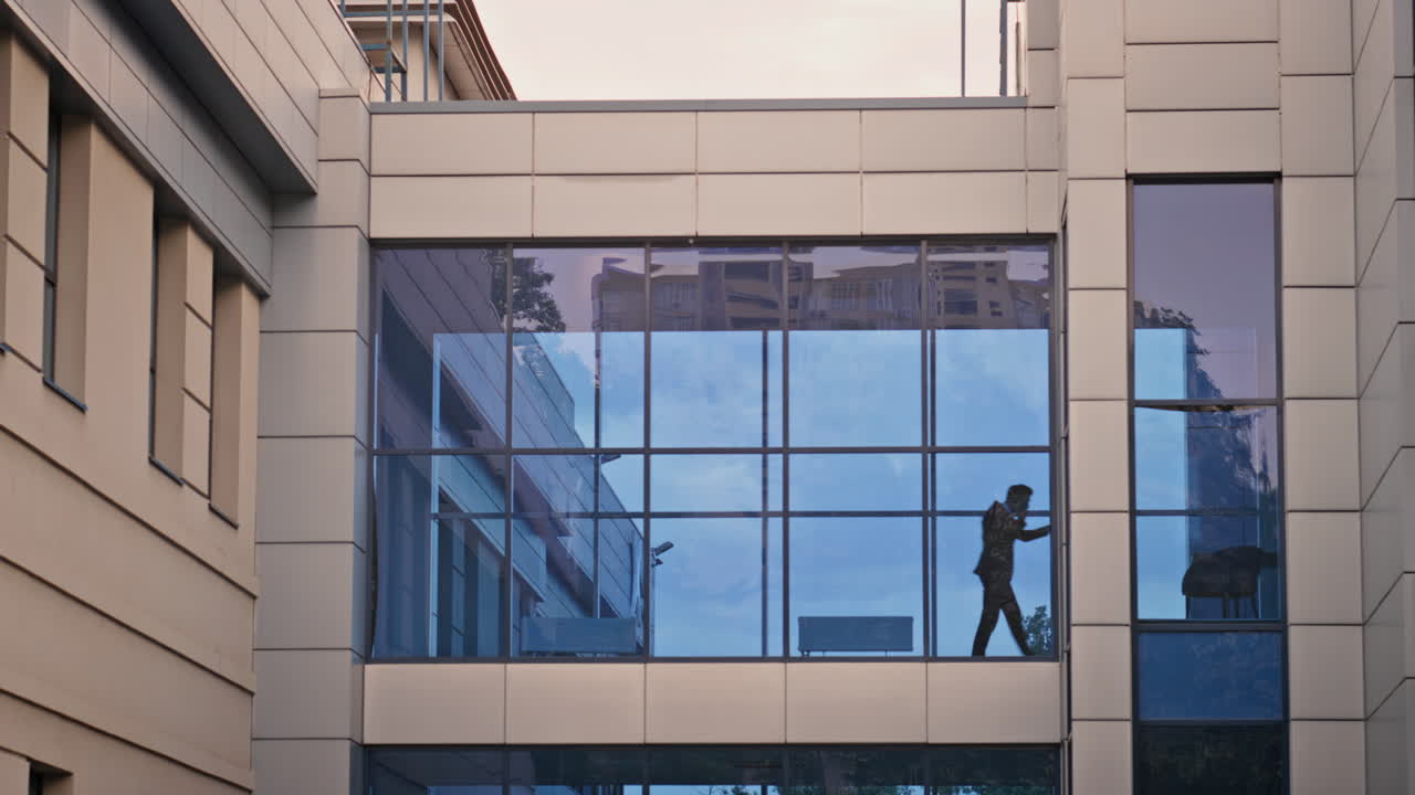 Silhouette manager walking inside glass office corridor talking cellphone
