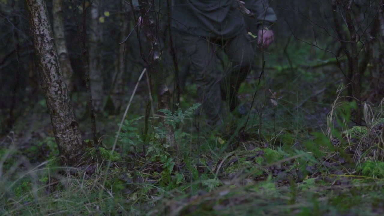 Lav vinkel optagelse af en løbende mand i naturen med rygsæk, der falder om på jorden i skoven.