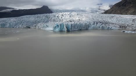 Luftaufnahme-Der-Eisberglagune-Von-Fjallsárlón,-Mit-Erstaunlicher-Türkisfarbener-Gletschernahe-Und-Unglaublichen-Eisformationen,-Umgeben-Von-Bergen-Und-Wolken-Im-Isländischen-Sommer