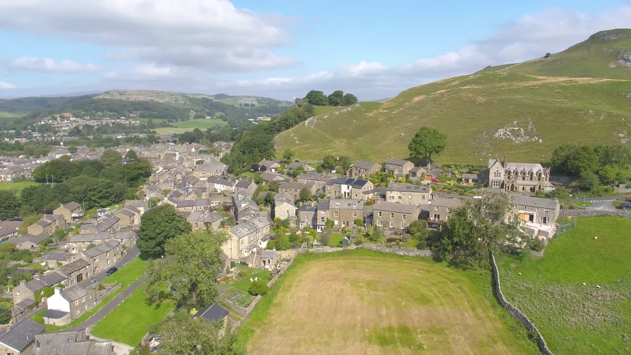 Drone footage, slowly reversing and panning revealing stone houses, dry stone walls, farmers' fields, hills and crags on the edge of Settle, a village in the rural countryside of North Yorkshire, UK