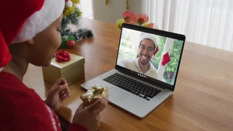 Mujer-Afroamericana-Con-Sombrero-De-Santa-Usando-Una-Computadora-Portátil-Para-Una-Videollamada-Navideña-Con-Un-Hombre-En-La-Pantalla