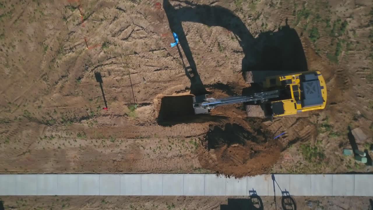 un zoom de giro lento de un dron de la vista de pájaro de una excavadora retroexcavadora que comienza a cavar un agujero y un sótano para la fundación de una nueva casa