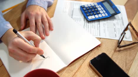 Hand-of-businesswoman-writing-on-book-at-desk