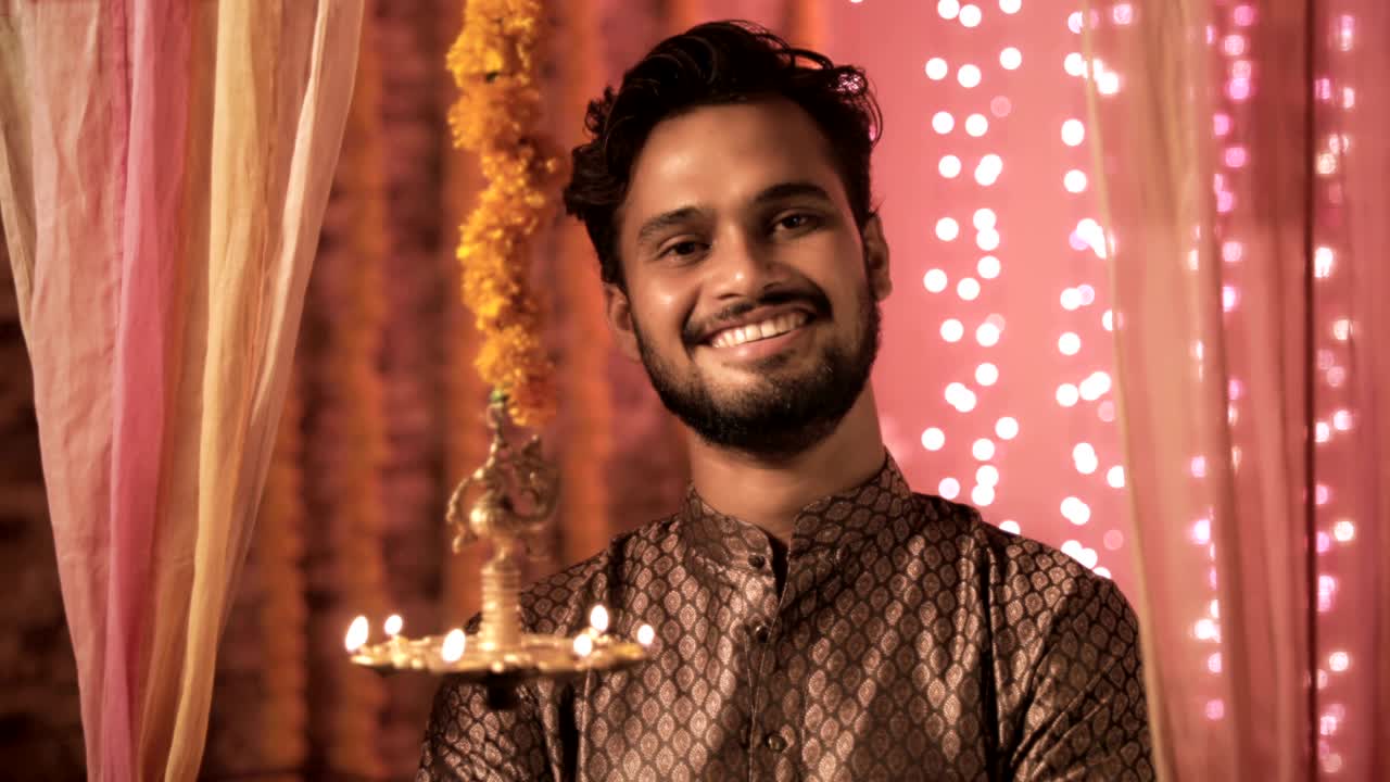 A handsome man wearing kurta smiles in a warm interior house decorated with lights and flowers