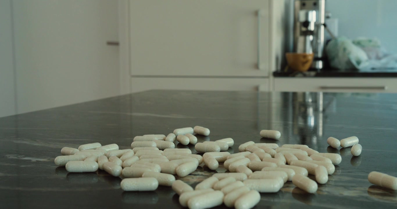 Primo piano di pillole bianche che cadono su un ripiano scuro della cucina, rappresentando farmaci, assistenza sanitaria, integratori, trattamenti, benessere, rischio di overdose, farmaci su prescrizione