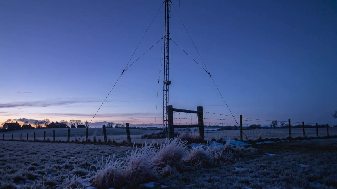 Pulling back camera revealing steel antenna mast and fence at frosty dawn, showing rural scene