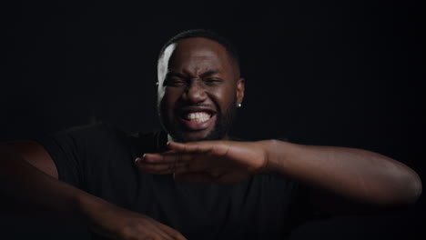 Joyful-african-man-making-movements-in-studio.-Afro-guy-singing-indoors.