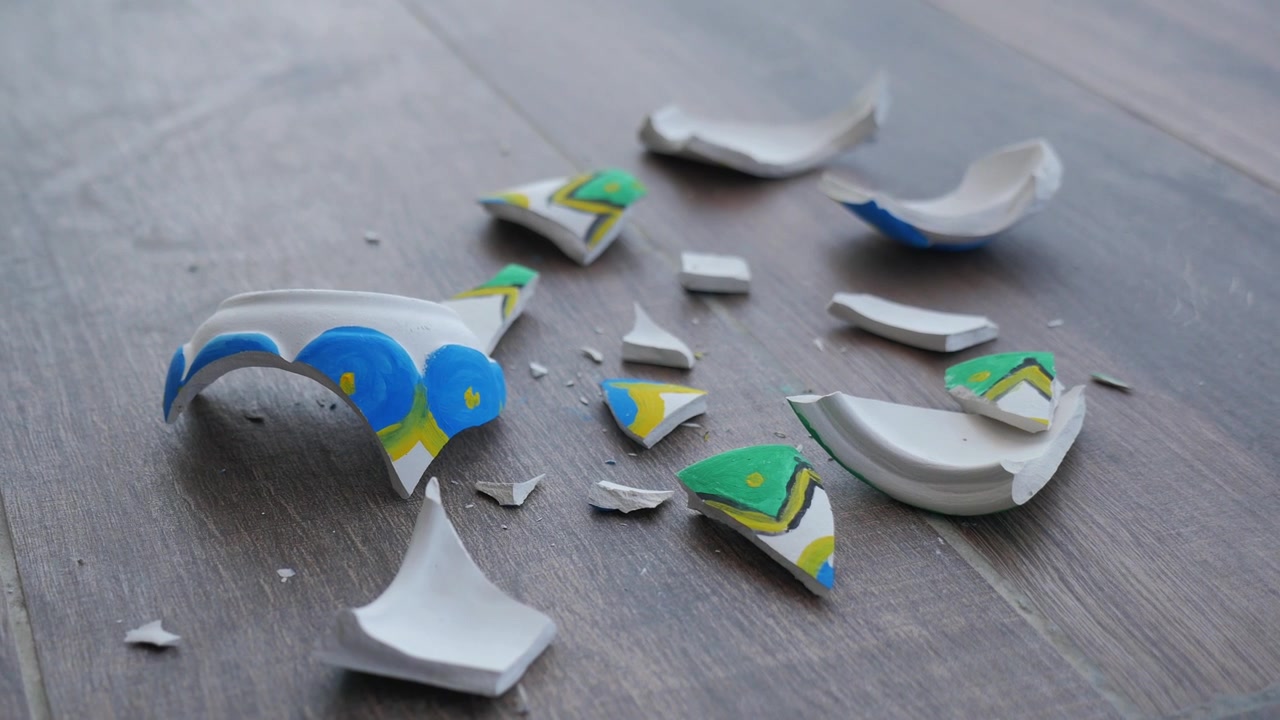 Broken Pieces of a Painted Ceramic Bowl on a Wooden Floor