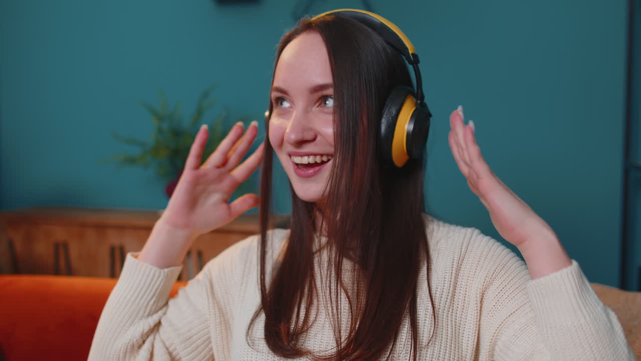 Overjoyed young woman in wireless headphones dancing singing on cozy couch in living room at home