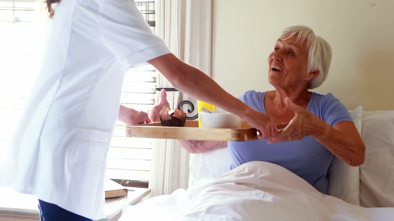 doctora que sirve desayuno a una mujer mayor en el dormitorio.
