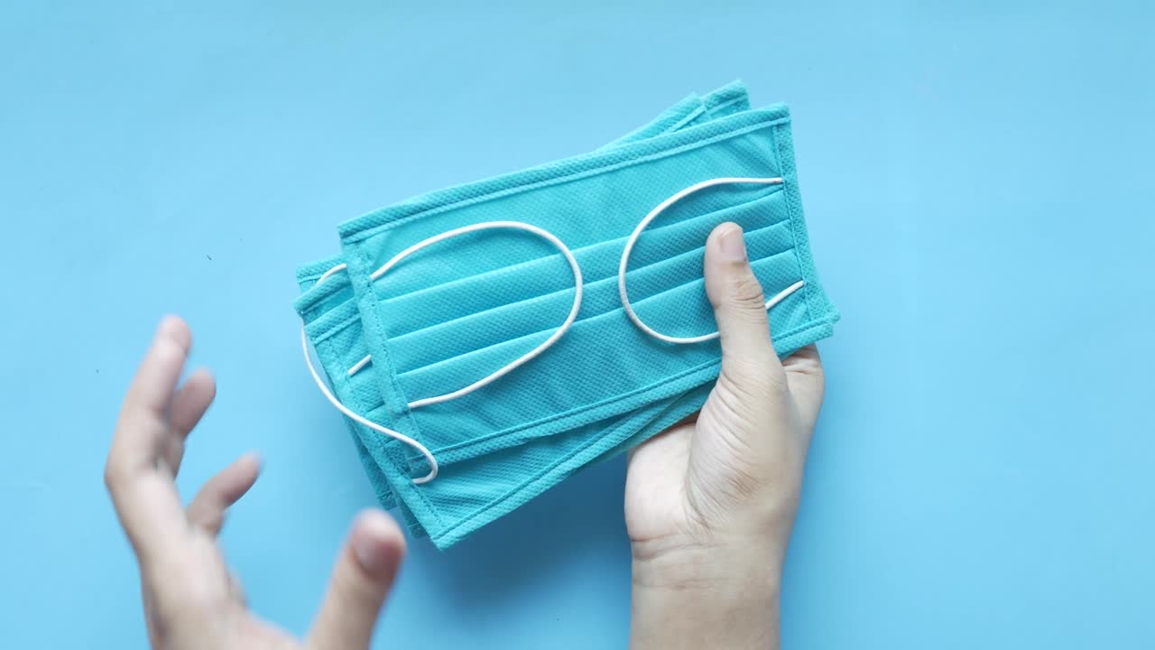 손은 파란색 얼굴 마스크의 더미를 들고 있습니다.