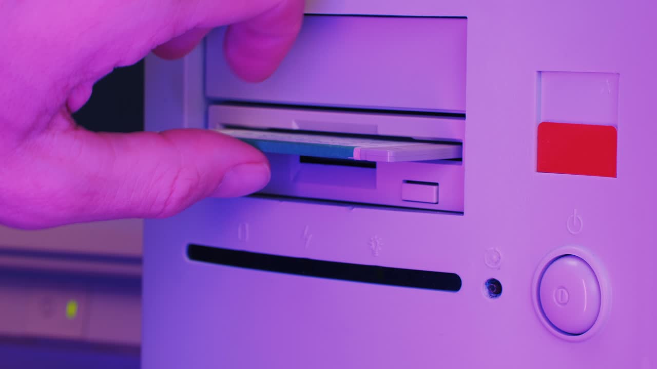 Hand inserting a floppy disk into a vintage computer