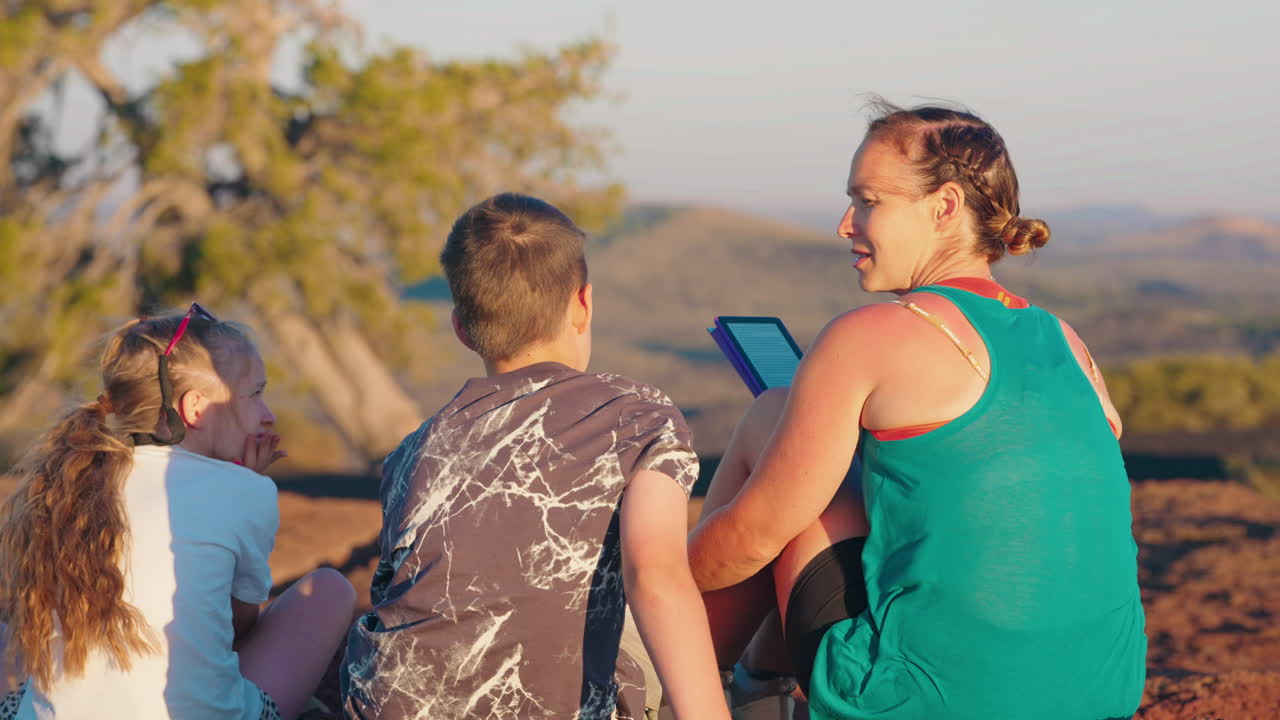 Family relaxing outdoors, reading an e-reader on a hilltop