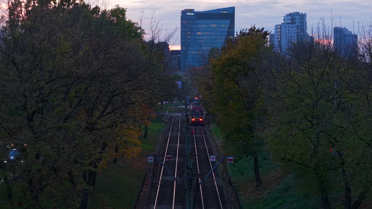 Warsaw, Poland. Aerial View of Tram on Railway Between Trees in Autumn Colors, Twilight in Modern City Neighborhood