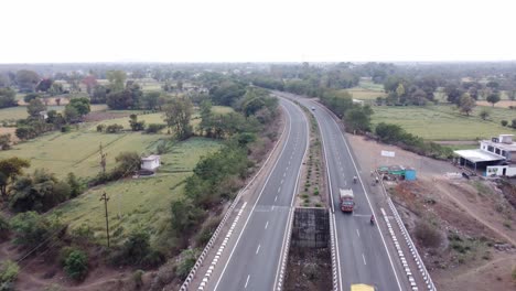 vista aérea de un avión no tripulado de una carretera nacional de la india de aspecto genérico y bien mantenida con paisaje rural de tierras de cultivo y árboles verdes exuberantes que pasan sobre un río seco