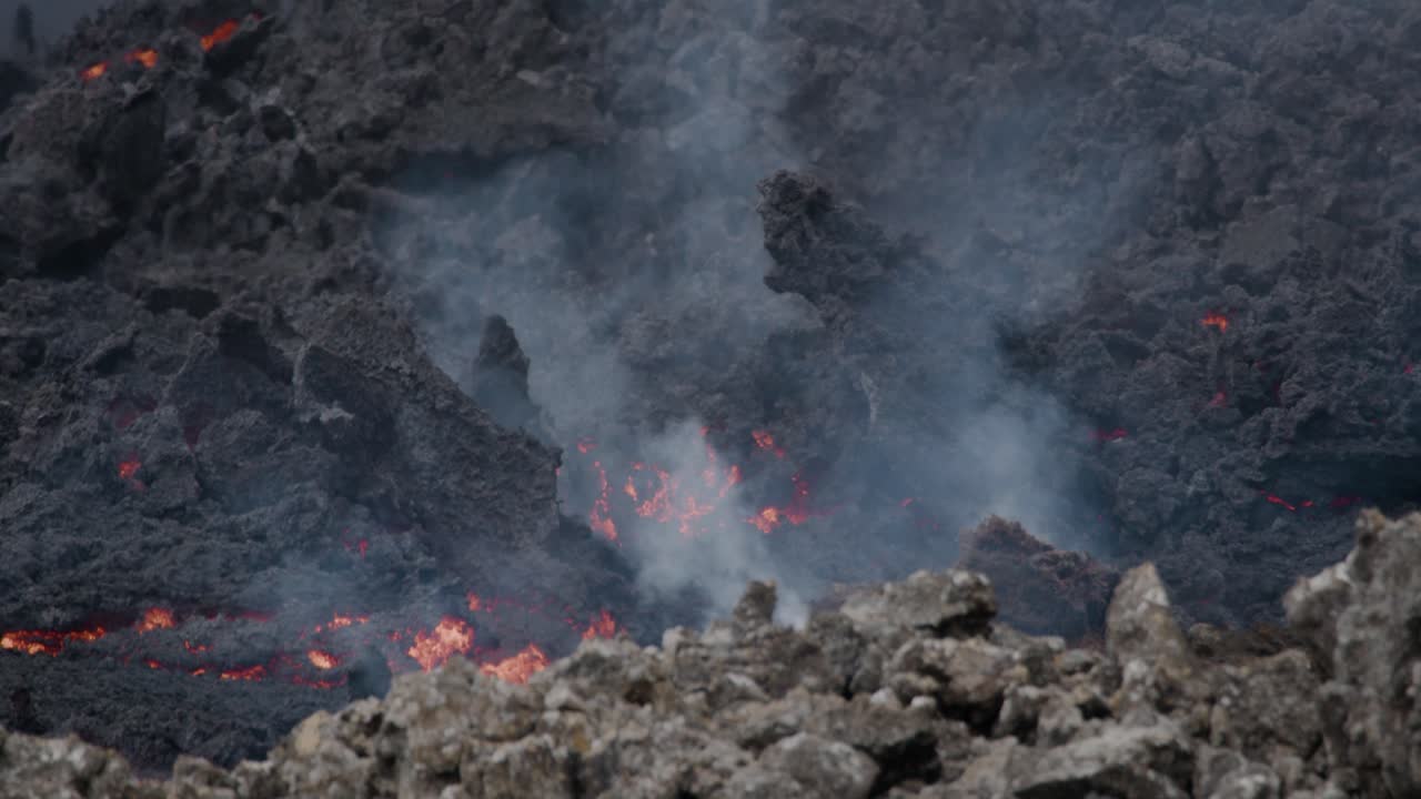 Smeltet lava, der langsomt flyder fra Grindavik vulkanen i Sundhnúkur krateret, Island, med røg der stiger op.