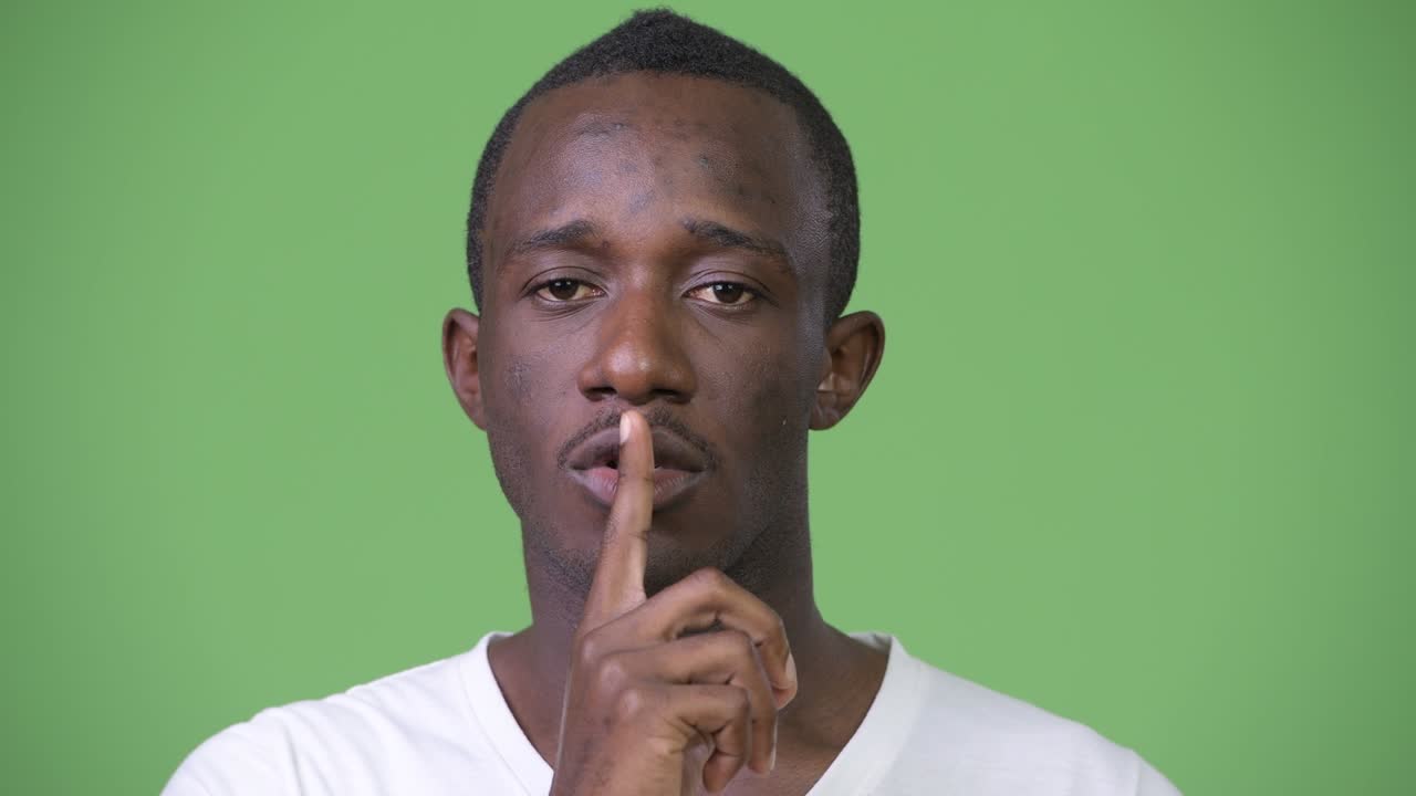 Giovane uomo africano con il dito sulle labbra su sfondo verde