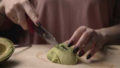 close-up of a woman’s hands slicing a ripe avocado on a wooden cutting board in a softly lit setting