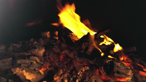 flames dancing in a dark firepit with a blazing pile of hot coals