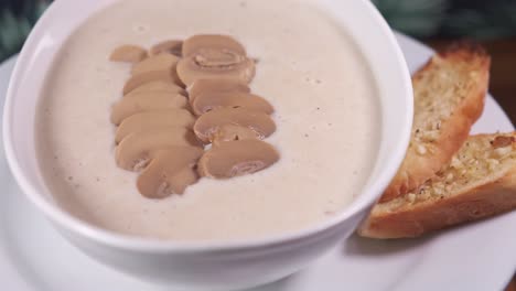 mushroom soup with freshly sliced mushrooms on top with two slices of garlic bread. close up spinning in white bowl