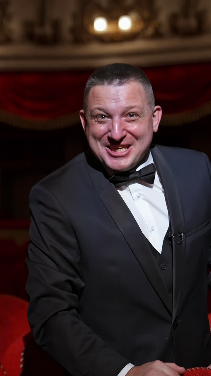 Man in empty theater hall points on a hand with watch and waits for performance beginning. Ready to watch visitor. Vertical video