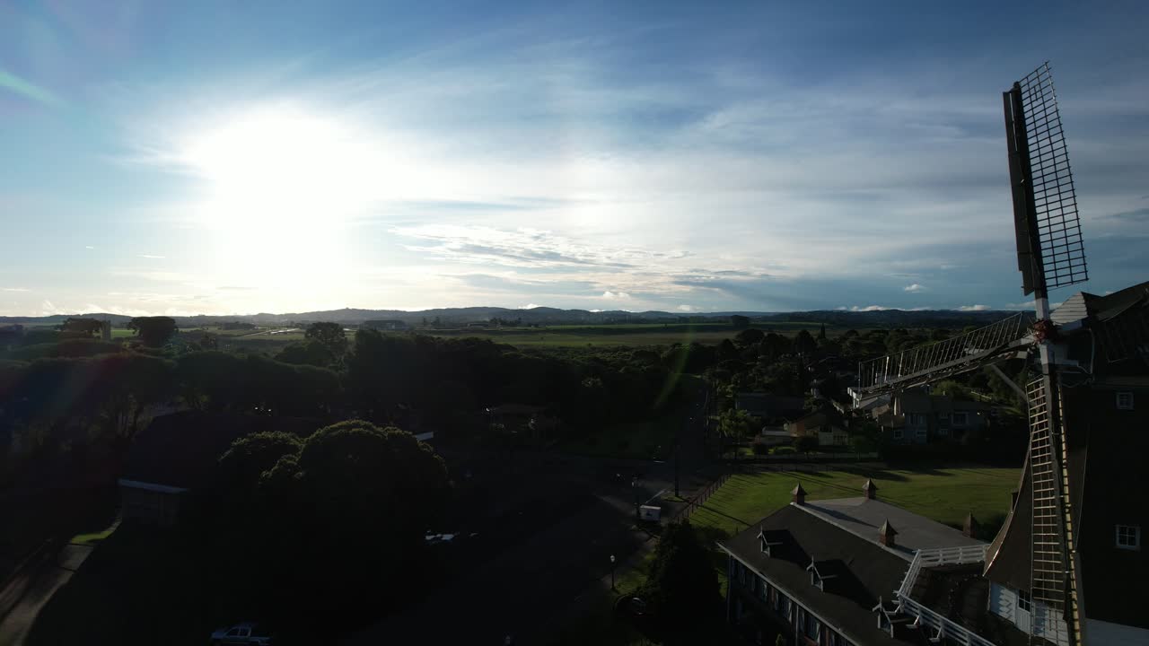 Traveling backwards revealing a beautiful windmill in Brazil, magical and soft light during the sunset, blue sky, replica of a Dutch windmill