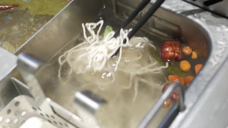 putting fresh handmade egg noodle intoboiled szechwan hotpot chinese style cuisine asian soup