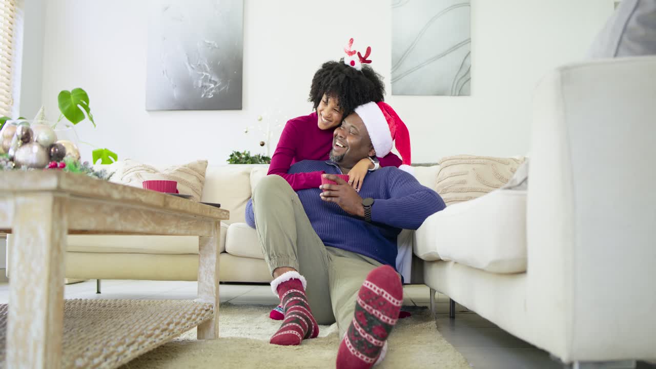 Diverse couple at home with woman approaching embracing partner while man sipping from red mug