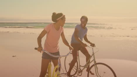 Lichtflecken-Gegen-Ein-Afroamerikanisches-Paar,-Das-Gemeinsam-Am-Strand-Fahrrad-Fährt