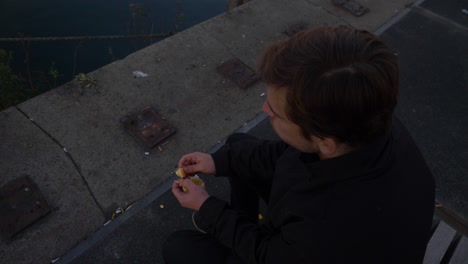 de arriba hacia abajo, arriba, cerca de un joven sentado en un banco y comiendo rodajas de naranja.