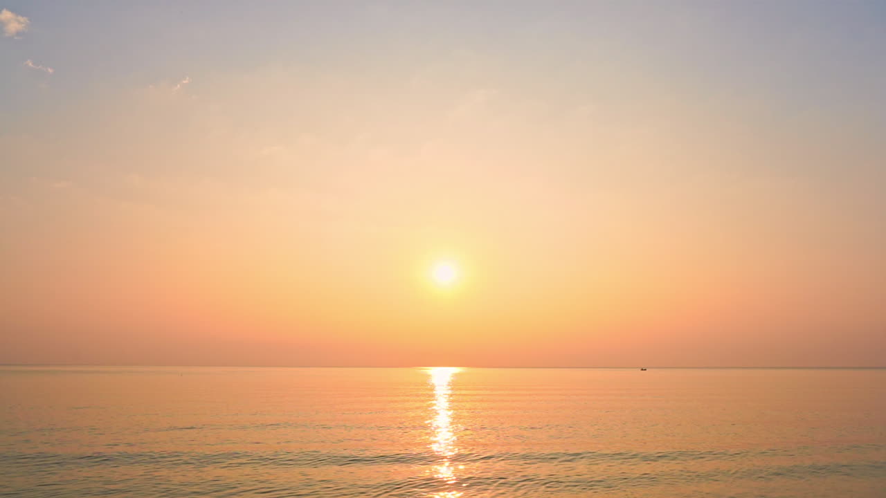 밝은 노란색 태양이 바다 지평선 위로 해질녘 분홍색과 노란색 하늘에 매달려 있습니다.