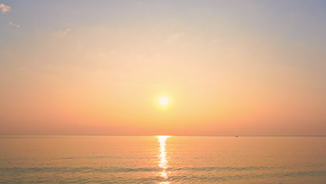 a bright yellow sun hangs in a pink and yellow sky at sunset over the ocean horizon