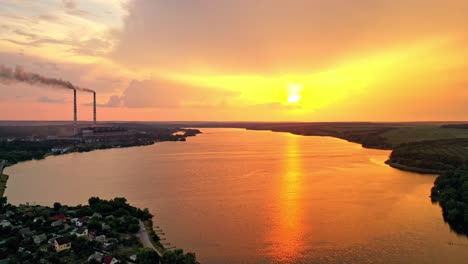 aerial landscape with sunset view over the river. beautiful evening river with sun reflection. two big pipes with smoke from the power plant near the water. camera moves right.