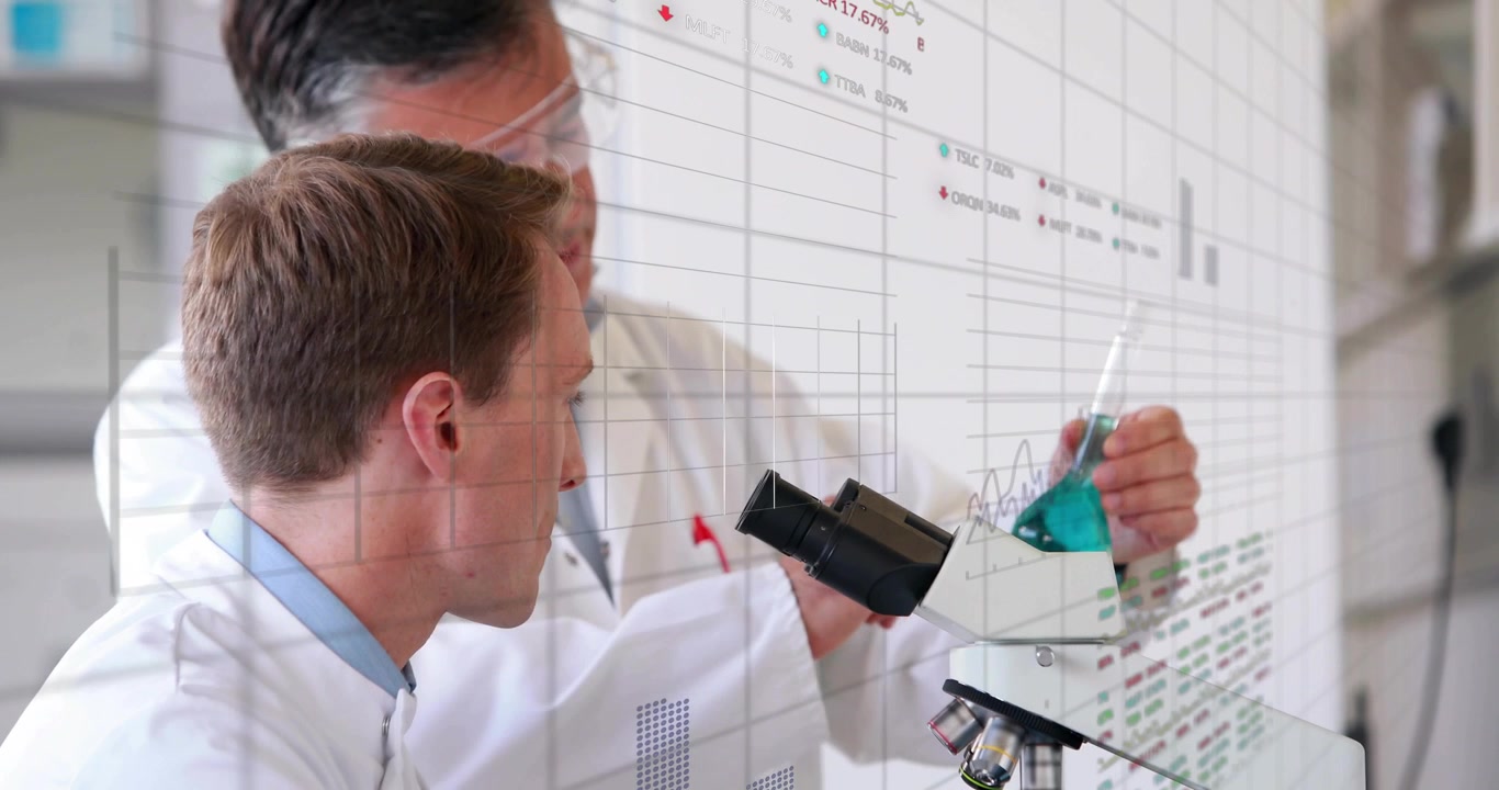 Lab tech peering microscope while senior moving flask closer and pointing, charts showing for study