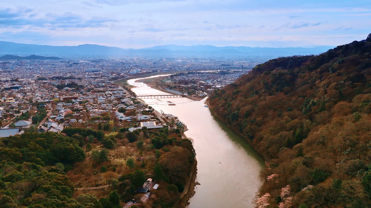 Flight above the narrow Katsura river in Kyoto, Japan. Vast cityscape surrounded by mountains at backdrop. Aerial view.