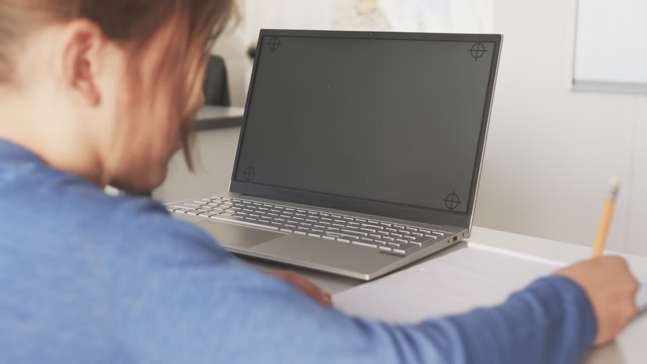 Using laptop and writing in notebook, student studying in school classroom, copy space