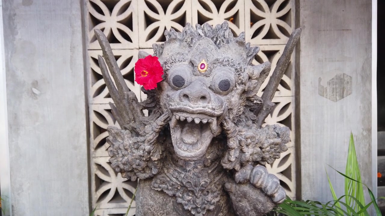 Primo piano di una statua tradizionale balinese di guardiano in pietra con fiore di ibisco rosso a Ubud, Bali