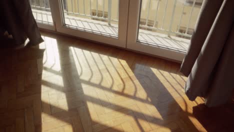 Sunlight entering from window creating shadows on wooden floor inside apartment. Bright daylight in summer. Room lit from outside. Hope and positivity concept. Green energy and innovative solutions