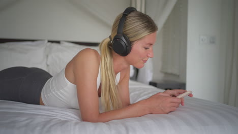 woman swaying head to rhythm of music while relaxing in comfy bed, scrolling phone