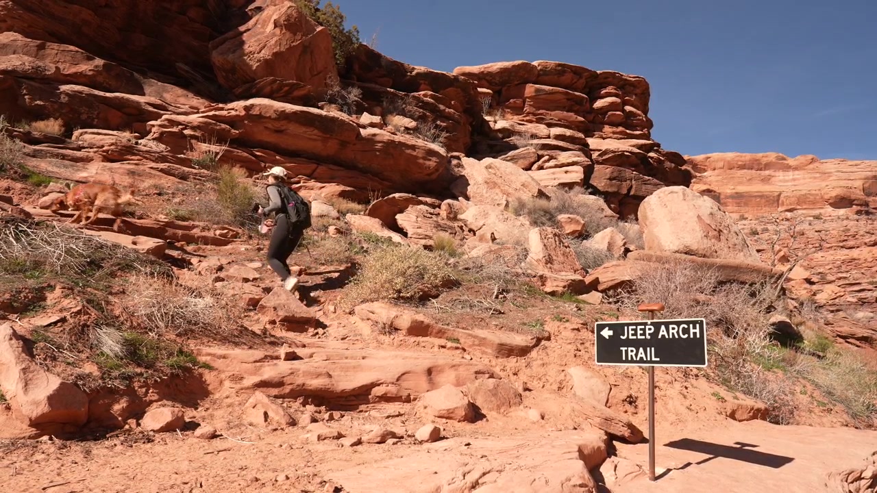 Donna con cane che passa davanti al cartello per il sentiero Jeep Arch, escursione panoramica da Moab, Utah, USA.