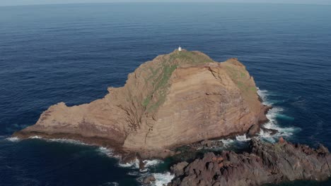 big rock in serene turqouise ocean with small lighthouse on top