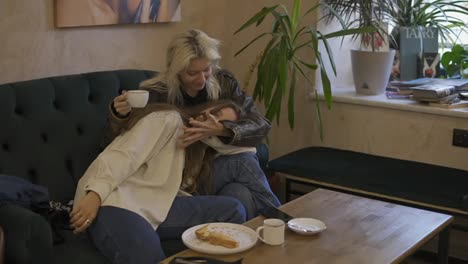 happy lesbian lgbtq couple in love cuddling, laughing, drinking coffee, having fun relaxing on couch at cafe